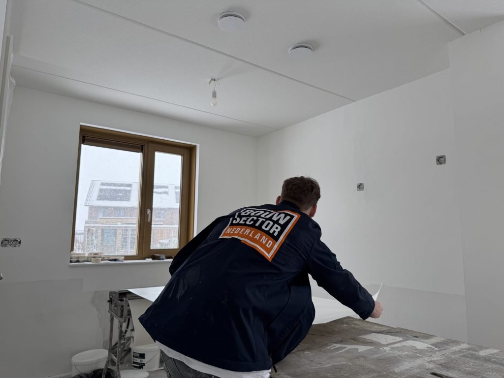 Behanger van Bouwsector Nederland buigt zich over de plaktafel in een lichte nieuwbouwkamer met een raam